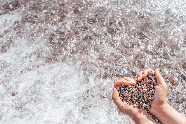 Woman hands holding small stones form heart shape background the sea