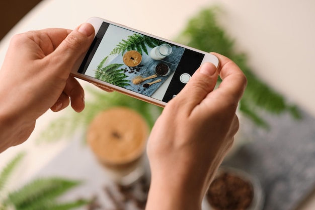 Woman hands making picture by phone for social media trendy fluffy Korean drink with whipped cream dalgona coffee with almond milk on marble board