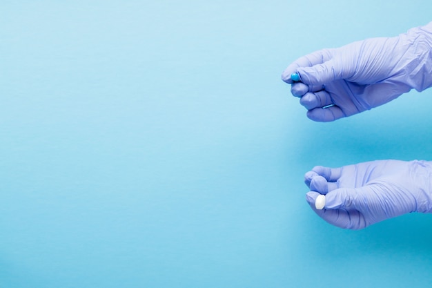 Woman hands in medical gloves giving two big pills. Blue and white. Make your selection. Copy space