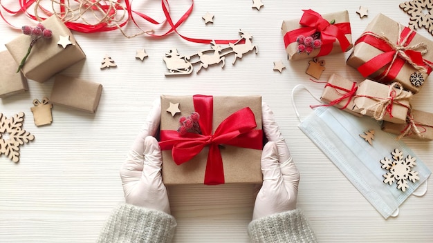 Woman hands in medical gloves hold Christmas holiday present in craft paper with red ribbon