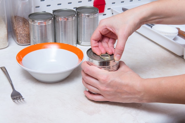 Woman hands opening tin can with canned tomatoes, kitchen table