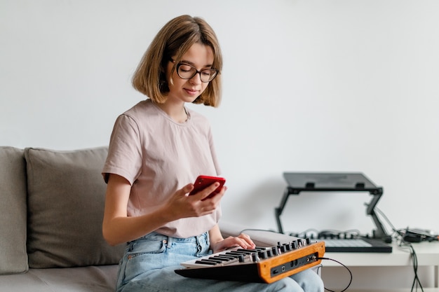 Woman hands playing minilogue synthesizer using mobile app at home