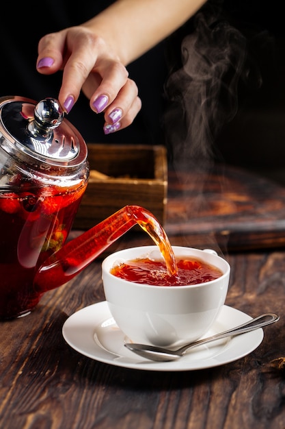 Woman hands pouring hot tea in a cup from pot