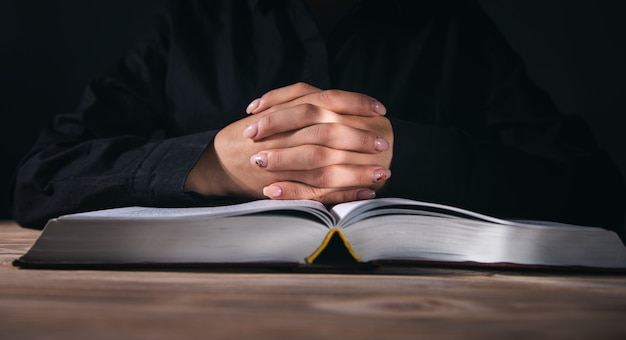 Woman hands praying with a Bible on dark room