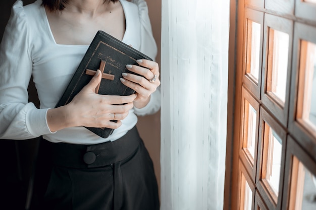 Woman hands praying with bible and wooden cross at church