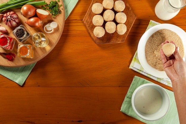 Woman hands preparing brazilian croquette coxinha de frango with bread crumbs on a wooden kitchen table Top view