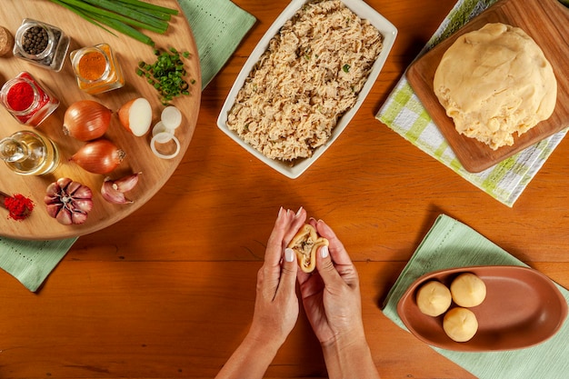 Woman hands preparing brazilian croquette coxinha de frango on a wooden kitchen table Top view