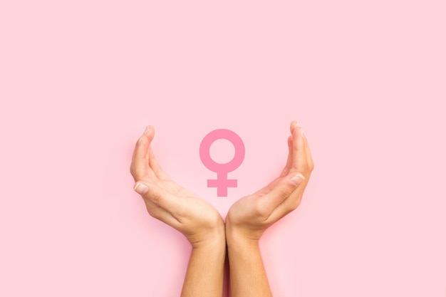 Woman hands protecting female sign on a pink background with copy space