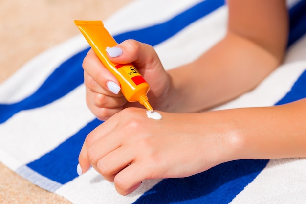 Woman hands putting sunscreen from a suncream bottle.