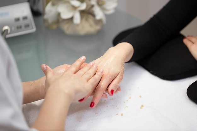 Woman hands receiving a hand scrub peeling by a beautician in beauty salon SPA manicure