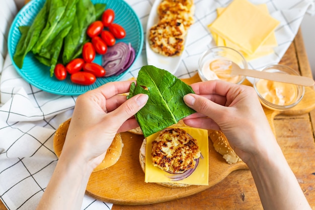 Woman hands take a burger roll and lay the salad on top of the cutlet.