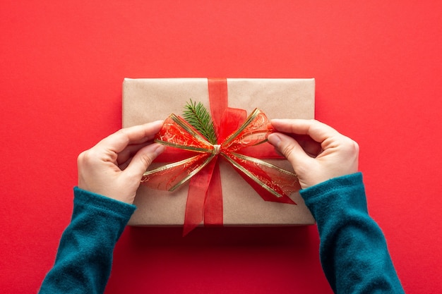 Woman hands tying a bow on Christmas present on red