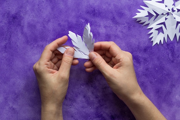 Woman hands unfolding paper to reveal snowflake on the violet surface