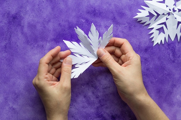 Woman hands unfolding paper to reveal snowflake on the violet surface