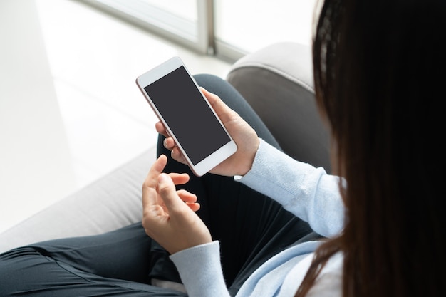 Woman hands using mobile phone while sitting on sofa in living room at home. Business, technology and lifestyle concept.