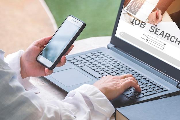 Woman hands using smartphone with laptop computer to searching for find jobs vacancies on internet