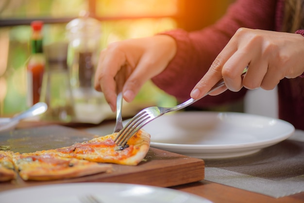 Woman hands using spoon and fork taking slices of pizza.