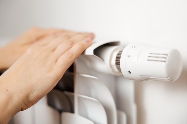 Woman hands on white heating radiator close up view It is cold person warms up Central heating system Heating is getting more expensive save money Energy crisis