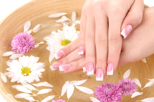 Woman hands with french manicure and flowers in bamboo bowl with water