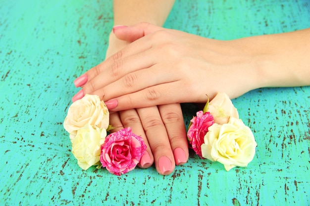 Woman hands with pink manicure and flowers on color background