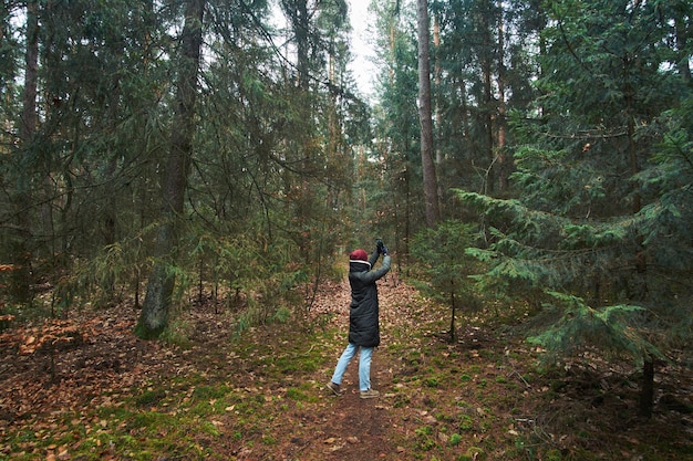 Woman has a walk in autumn forest and making photos on smartphone