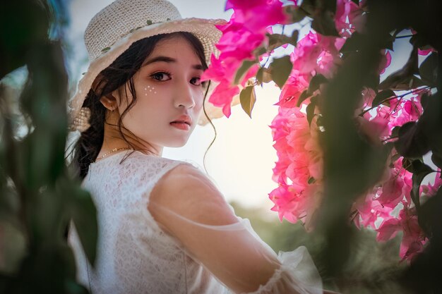 A woman in a hat stands in front of a bougainvillea flower