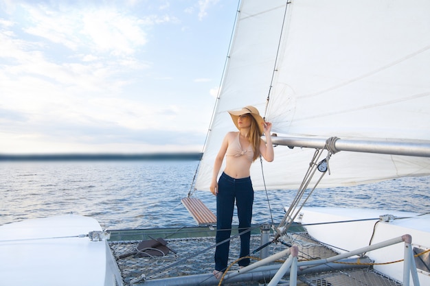 A woman in a hat on a yacht, against the sky and sea.