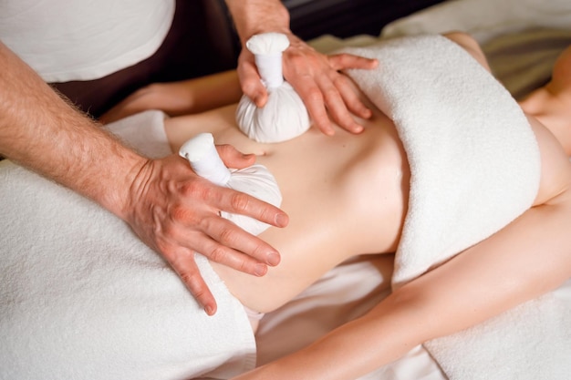 Woman having an abdomen massage with with aromatic herbal bags