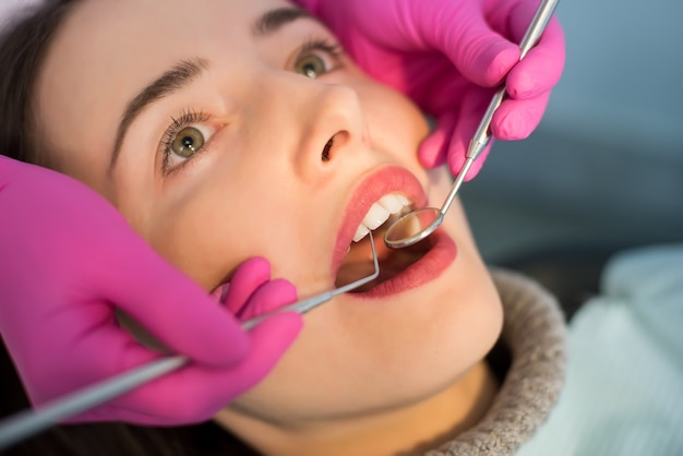 Woman having dental check up in dental office. Dentist examining a patient's teeth with dental tools - mirror and probe