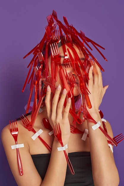 Woman having her face covered in plastic forks and spoons