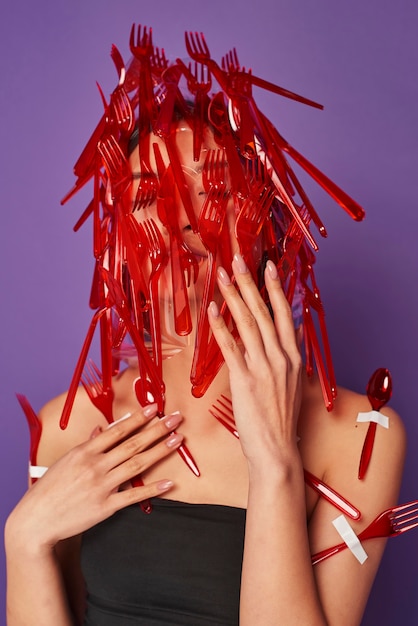 Woman having her face covered in plastic spoons and forks