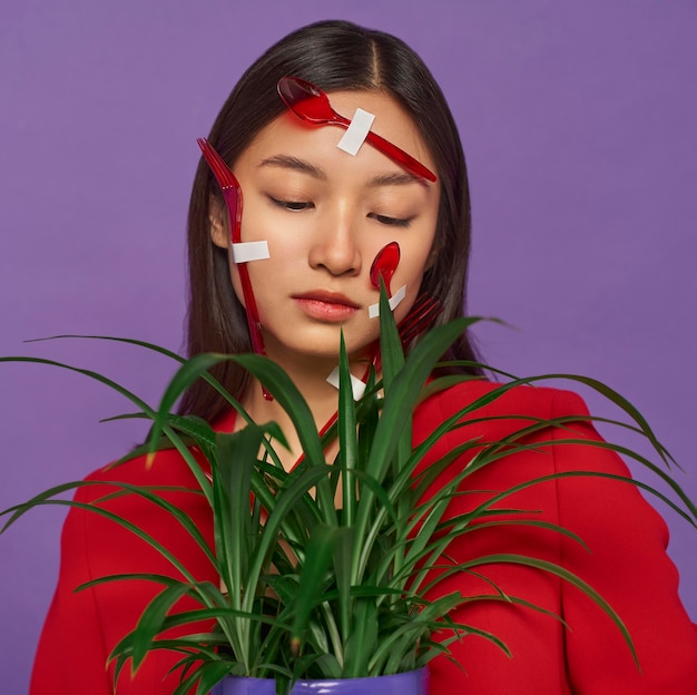 Woman having her face covered in plastic spoons while holding a plant