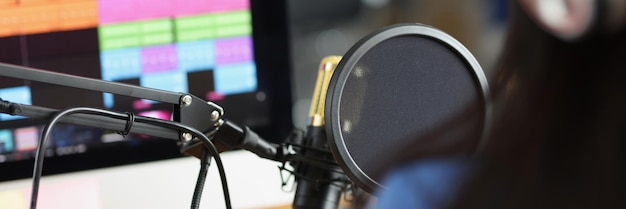 Woman in headphones in front of microphone looks at monitor with sound track radio host