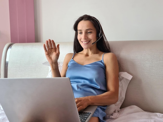 Woman in headphones with microphone lies on bed and works on laptop