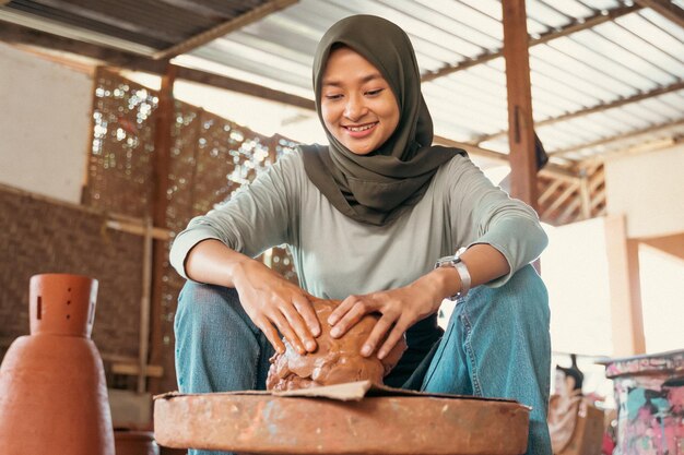 Woman in headscarf sitting relaxed holding wet clay on wheels