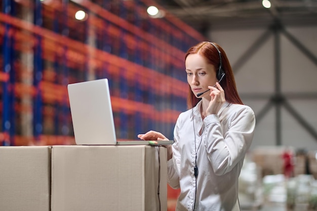 Woman in headset standing near laptop in warehouse