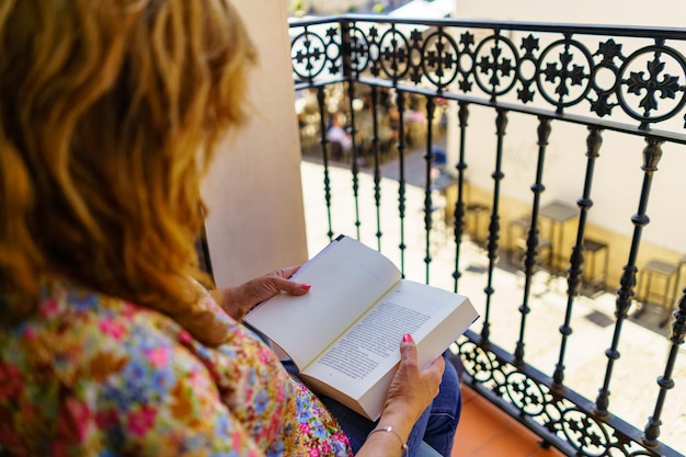 A woman on her back reading a book on the terrace of her houses on a sunny and hot day