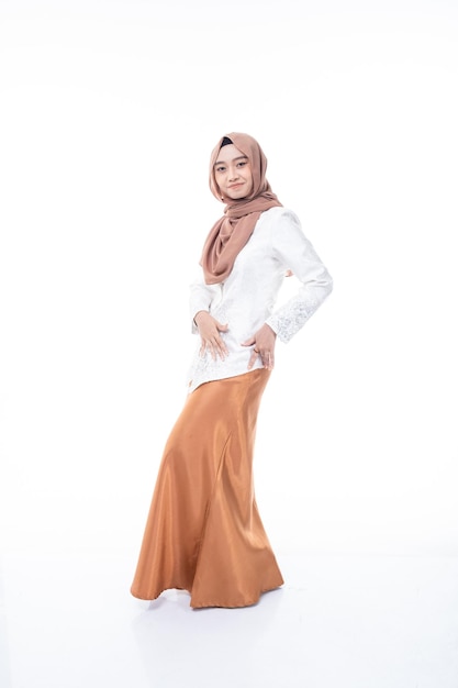 A woman in a hijab and a white shirt is standing in front of a white background.