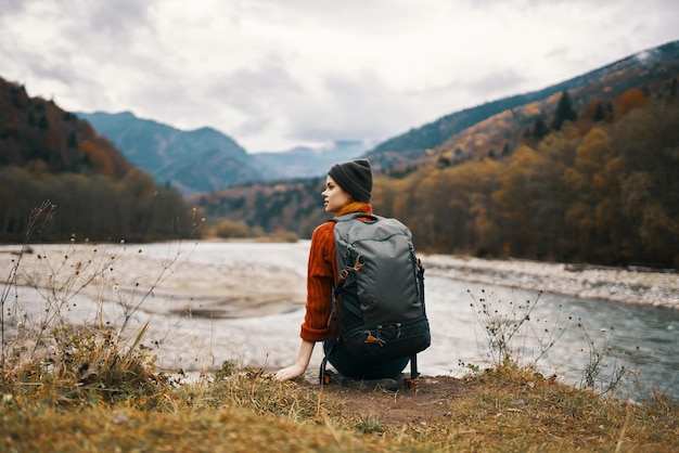 Woman hiker on the banks of the river in autumn and mountains in the distance clouds weather nature High quality photo