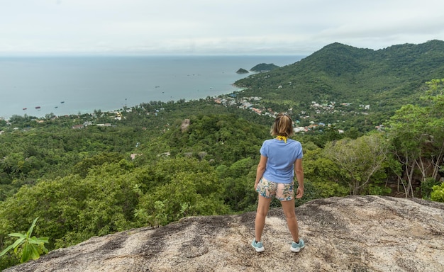 Woman hiker stands on the cliff with backpack and watching the seascape