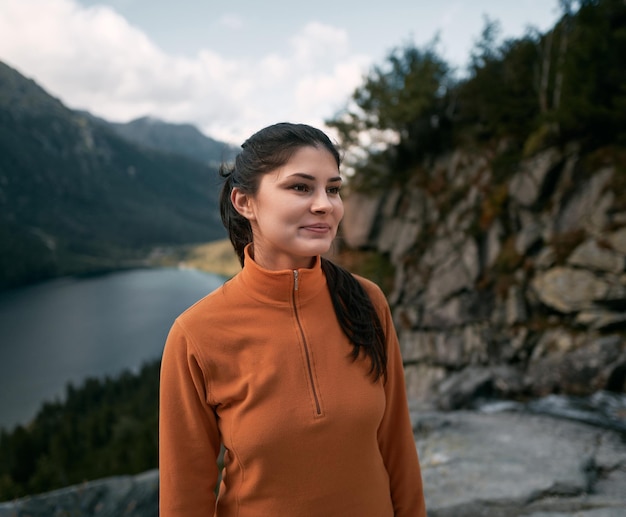 Woman hiker on the top of the mountain Concept of adventure vacations Traveler millennial girl is staying on the cliff edge with autumn forest and enjoying beautiful valley view