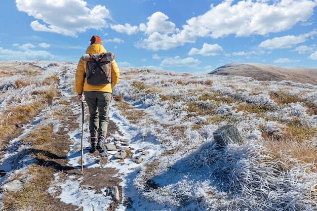 Woman hiker in yellow down jacket goes on the snowy slope of mountain ridge against mountains and st