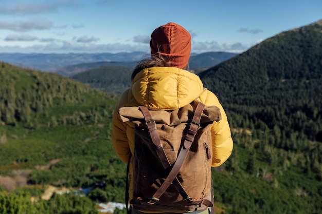 Woman hiker in yellow jacket with backpack hiking green forest mountains at sunny autumn day