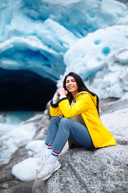 Woman hiking at glacier enjoys freedom Girl tourist in yellow jacket near large glacier