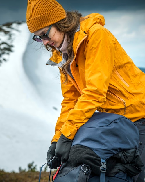 Photo woman hiking in snowy mountain area wearing cold weather accessories wind jacket and backpack for camping outdoor she opening her backpack female portrait lifestyle