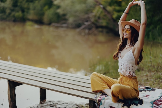 Photo woman in hippie hat smiling and doing yoga meditating in the lotus position in the sunset light