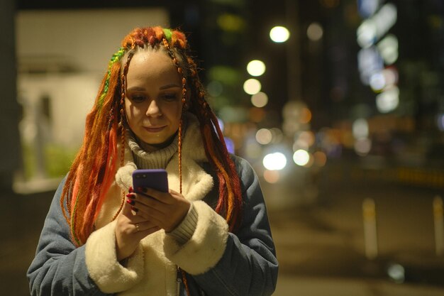 Woman hipster with smartphone at night in city