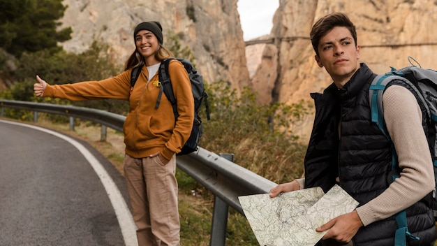 Woman hitch-hiking for a car and man holding map