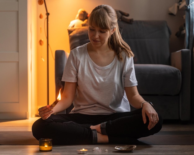 Woman holding aromatic saldanwood stick while meditating in cozy evening at home