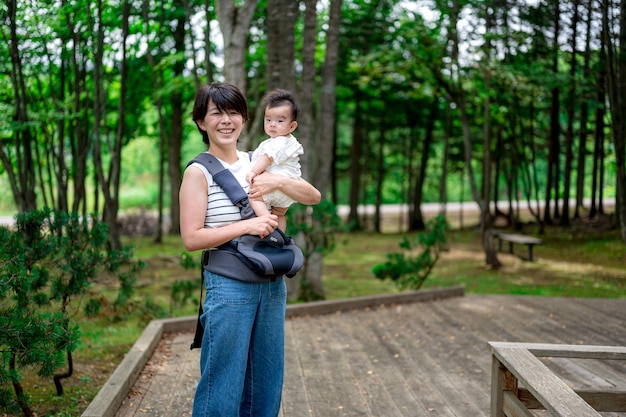 A woman holding a baby in a carrier in a forest